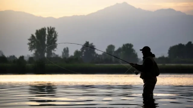 A serene lake scene with an angler casting a line, symbolizing a catfishing adventure.