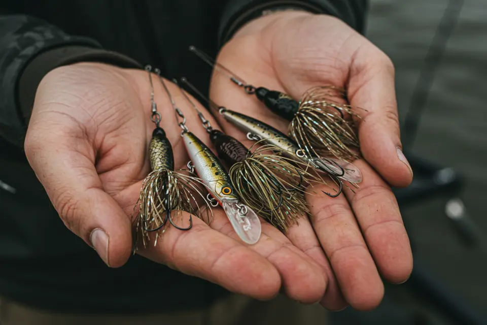 A fisherman holding a selection of fishing lures, focusing on their details in an outdoor setting. 