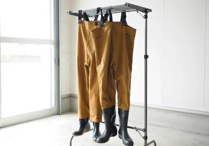 Breathable fishing waders properly hanging upside down on a rack to dry, illustrating essential wader care and storage.