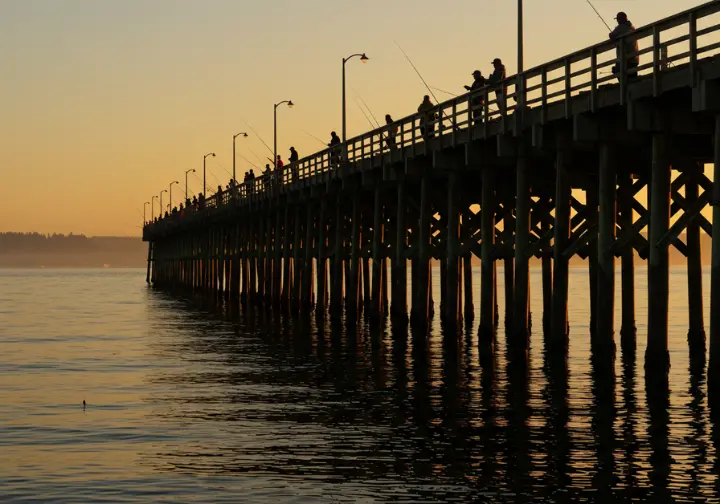 Anglers fishing at Edmonds Pier during sunrise, with the Puget Sound in the background.