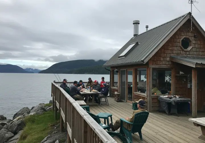 Anglers enjoying a meal at a cozy fishing lodge on Kodiak Island, overlooking the water.