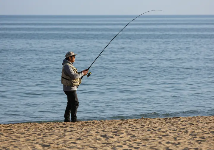 An angler casting a fishing rod on a beach, symbolizing the start of a Cabo fishing quest.