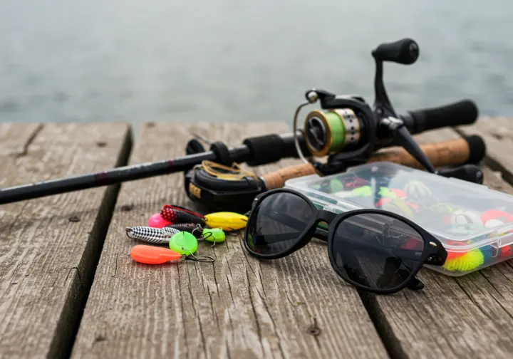 Close-up of essential fishing gear, including rod, reel, tackle box, and sunglasses, representing gear and techniques for Cabo fishing.