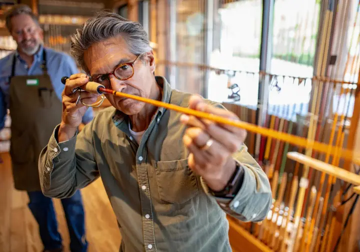 Person carefully inspecting the condition and straightness of a vintage bamboo fly rod before buying.