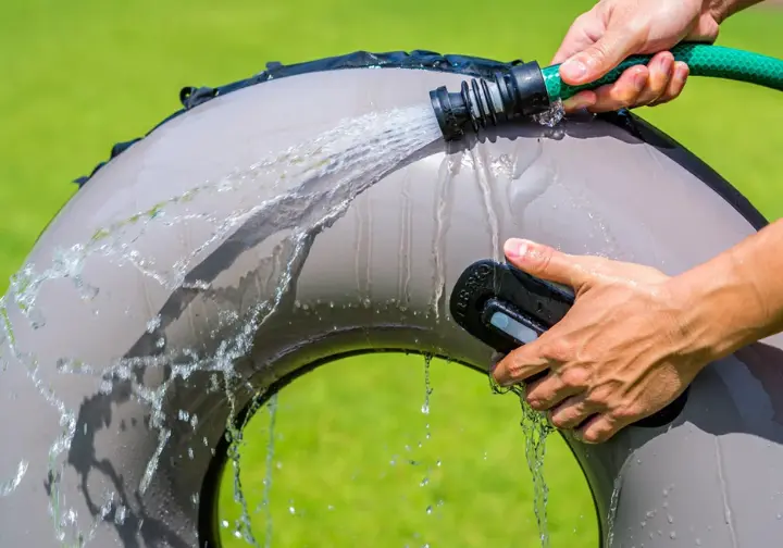 Hands carefully rinsing a float tube with fresh water from a hose, demonstrating proper cleaning and maintenance.