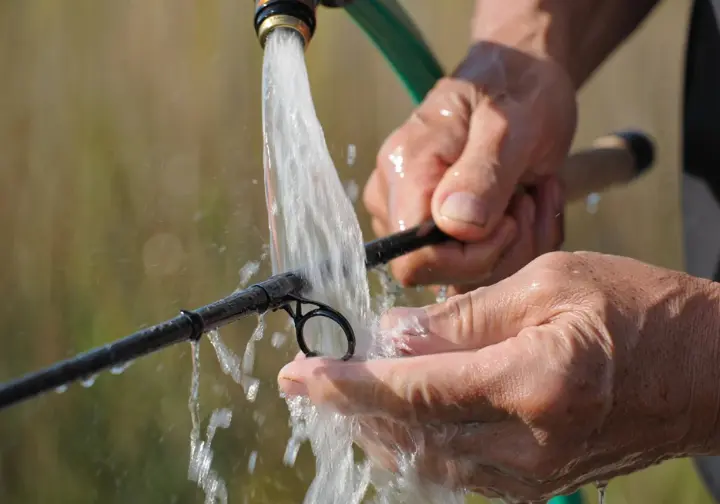 Hands carefully rinsing a fishing rod with fresh water after use, illustrating essential rod care for maintenance.