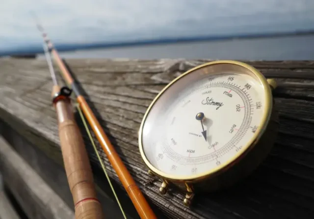 Barometer showing falling pressure next to a fishing rod on a pier, representing the myth vs reality of its effect on fishing.