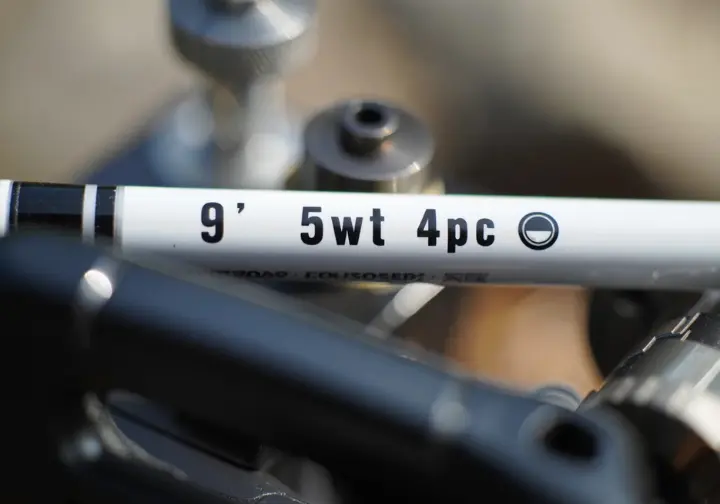 Close-up showing fly rod specifications like length and weight printed on the blank for decoding.