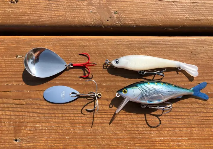 Flat lay of top lures for lake trout including spoon, spinner, jig/plastic, and crankbait on a dock.