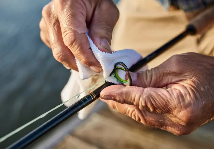 Angler carefully cleaning a saltwater fishing rod with a cloth after rinsing to protect the investment.