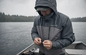 Best Rain Gear for Fishing and Why Cheap Sets Fail Angler in rain gear for fishing retying a lure in steady rain at the stern of a small aluminum boat