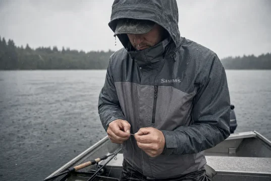 Best Rain Gear for Fishing and Why Cheap Sets Fail Angler in rain gear for fishing retying a lure in steady rain at the stern of a small aluminum boat
