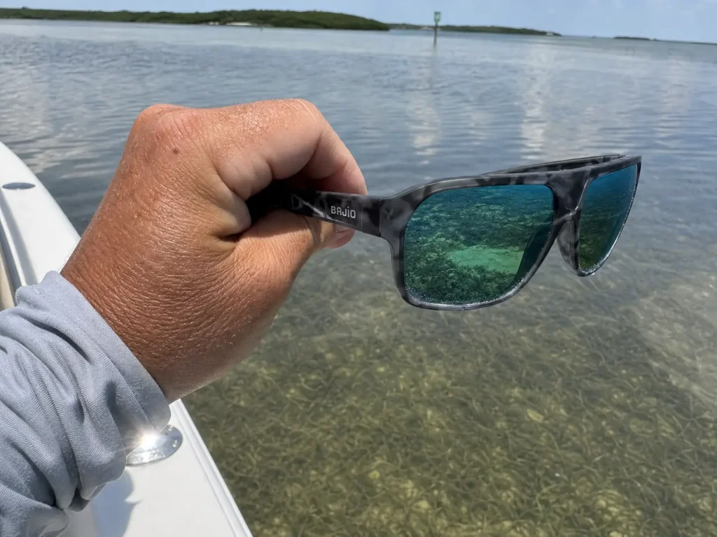 Polarized fishing sunglasses held over the water showing the grass bottom through surface glare