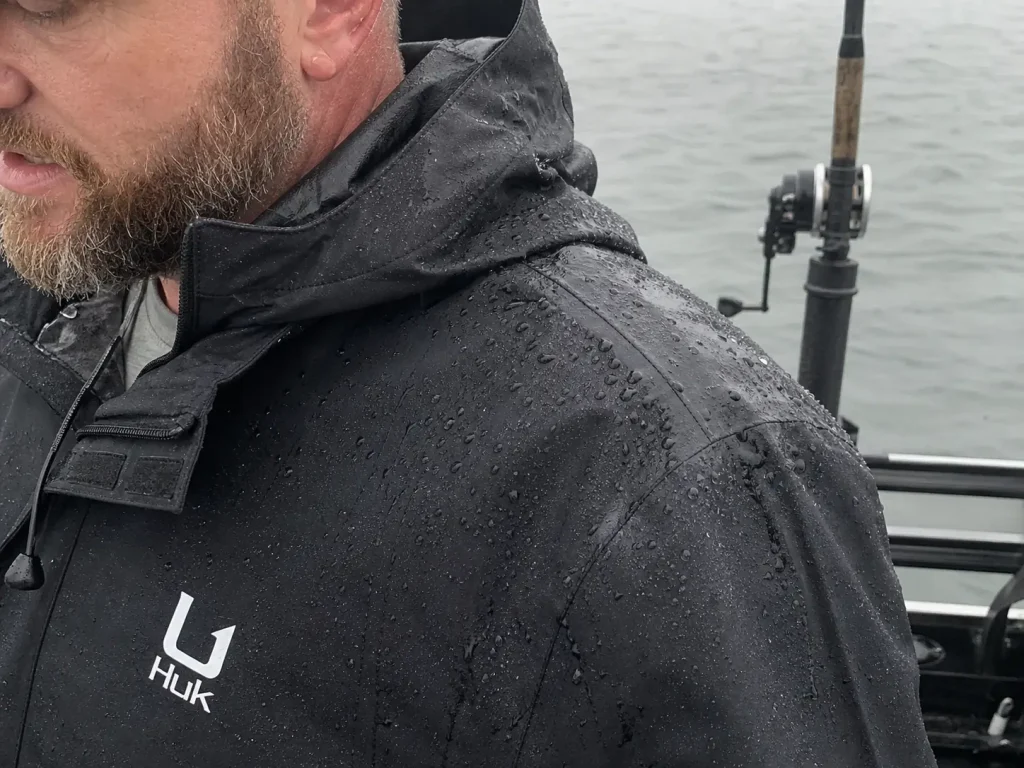 Close-up of rain beading on the shoulder seam of a waterproof fishing jacket on the water