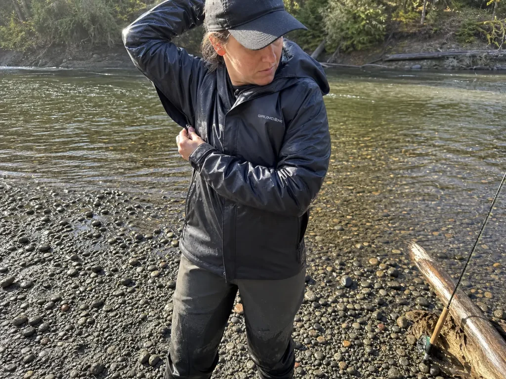 Woman angler opening the pit zip of a breathable fishing rain jacket during a break in the rain