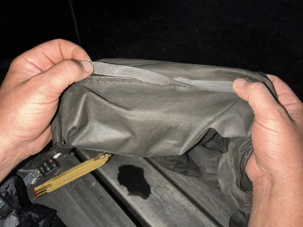 Hands inspecting peeling seam tape inside a cheap fishing rain jacket turned inside out at dusk