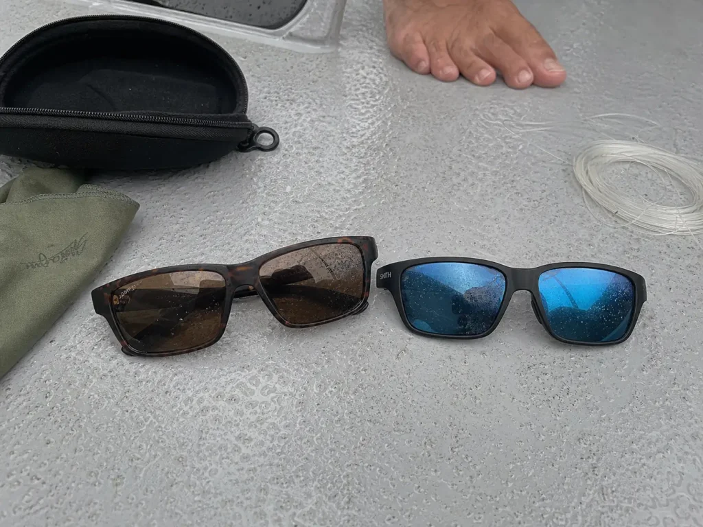 Glass and polycarbonate polarized fishing sunglasses side by side on a boat deck for comparison