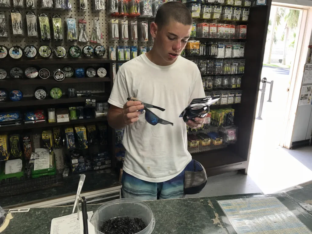 Angler comparing entry level and mid tier polarized fishing sunglasses at a bait shop counter