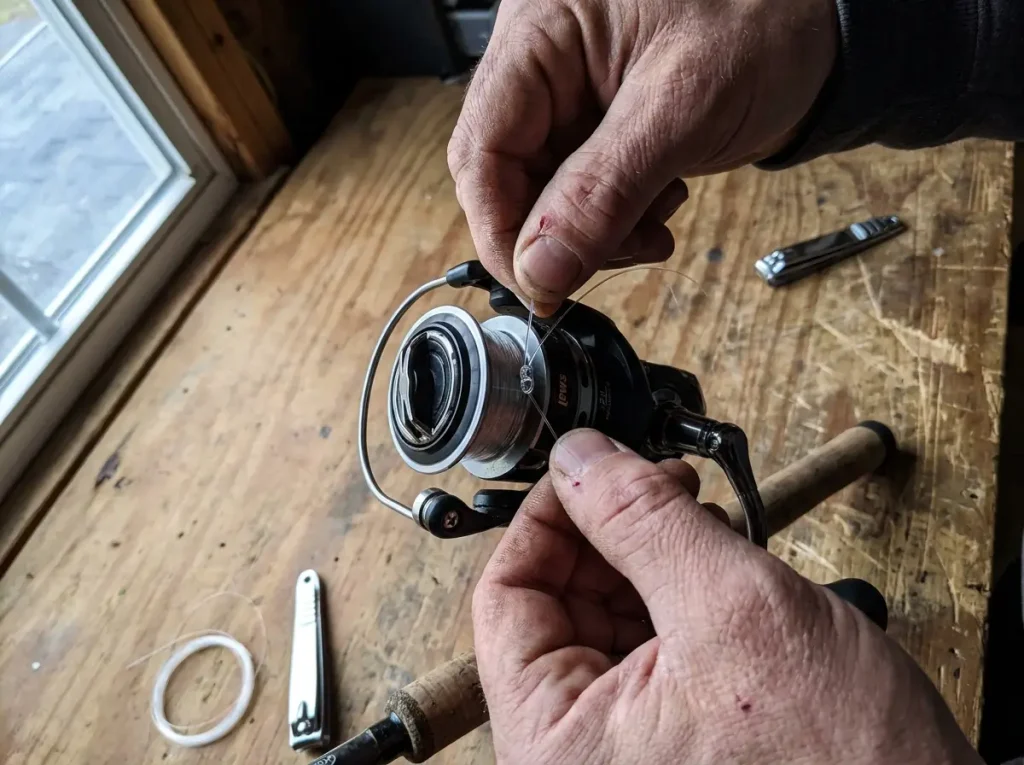 Hands tying an arbor knot to the spool of a Lew's reel before spooling line