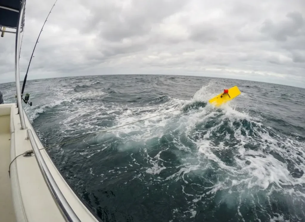 A yellow planer board skipping over waves at the end of a long fishing line, extending the trolling spread.