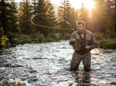 Beginner’s Guide to Fly Fishing: From Setup to First Cast An angler wading in a river casting a fly rod with a yellow fly line looping in the air during sunset.