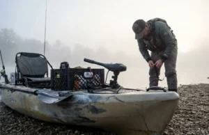 Best Fishing Kayaks Under $1000: Mod-Ready Rated A fully rigged fishing kayak sits on a gravel bank at sunrise with an angler preparing for a fishing trip.