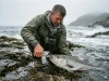 Best Fishing Pliers That Won’t Rust Shut Angler using titanium fishing pliers to back a hook out of a striped bass at the water's edge