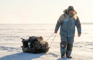 Best Ice Fishing Lakes Minnesota: Maps & Gear Guide A dedicated ice angler pulling a sled across the frozen, snow-covered surface of a large Minnesota lake at sunrise.