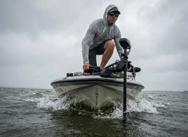 best-trolling-motor-guide-boat-electronics Angler on the bow of a bass boat using a trolling motor to fight heavy wind and waves.