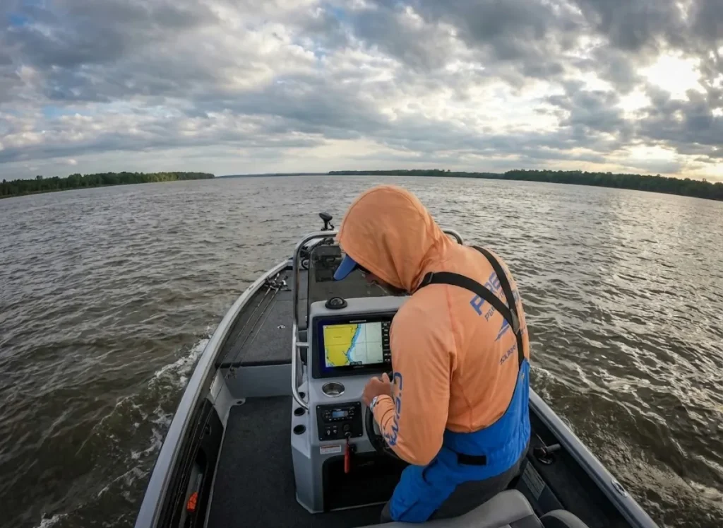 An angler in a boat on a large border river checking a GPS chartplotter to ensure they are in legal waters.