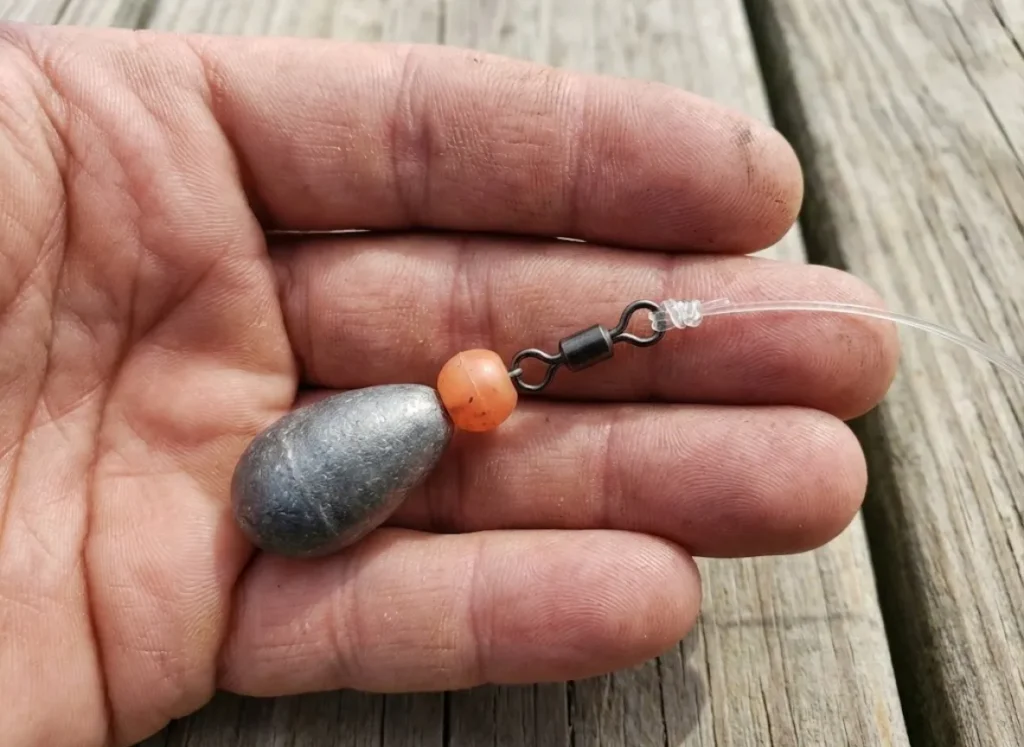 Close-up of a hand holding a Carolina fishing rig showing the sliding egg sinker, bead, and swivel components.