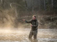 How to Cast a Baitcaster: The Zero-Backlash System Angler wading in a river executing a powerful cast with a baitcasting rod at sunrise.