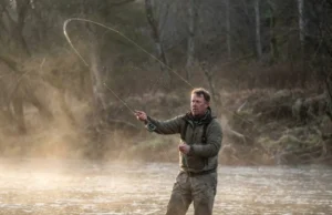 How to Cast a Baitcaster: The Zero-Backlash System Angler wading in a river executing a powerful cast with a baitcasting rod at sunrise.