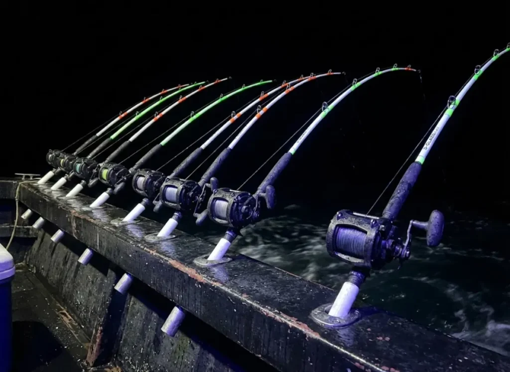 A row of heavy duty fishing rods on a boat at night with tips glowing under blacklight.