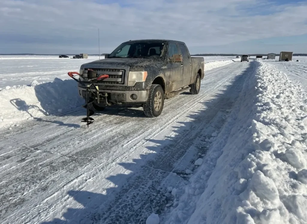A pickup truck driving along a plowed ice road on a frozen Minnesota lake.