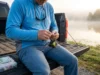 What Gear To Start Fishing: The Essential Beginner Checklist Angler sitting on a truck tailgate at sunrise preparing a spinning rod and reel for a fishing trip.