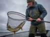Fall Fishing for Pike: The Temperature Playbook Angler in cold weather gear lifting a large northern pike in a net on a gloomy autumn day.
