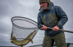 Fall Fishing for Pike: The Temperature Playbook Angler in cold weather gear lifting a large northern pike in a net on a gloomy autumn day.