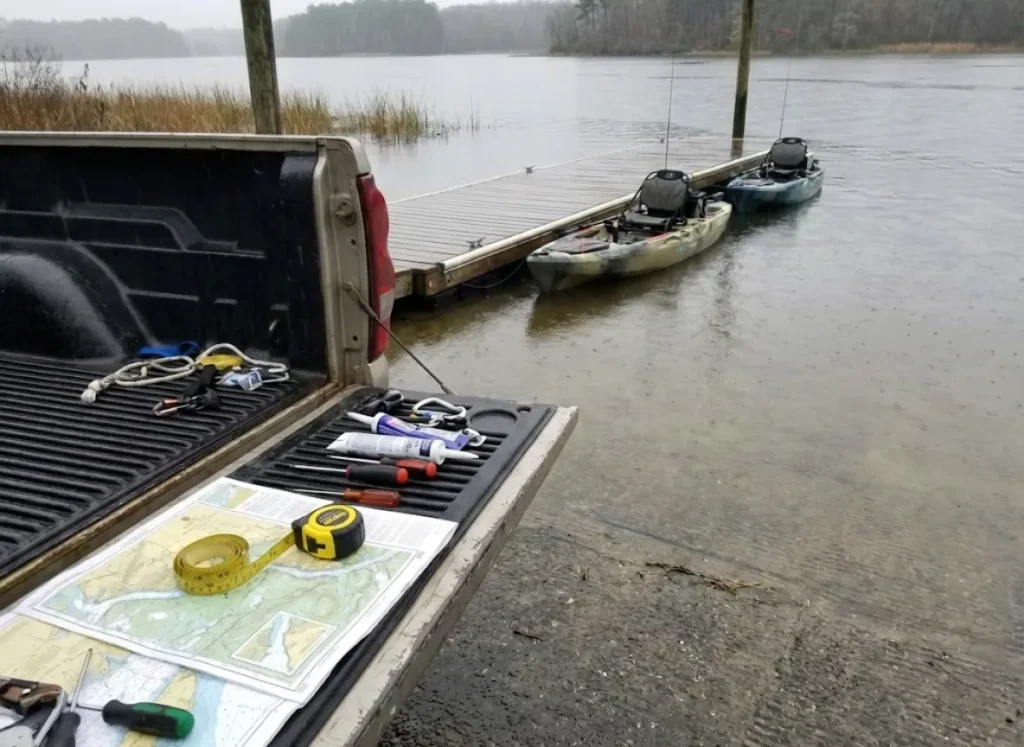 A tailgate covered in tools and maps with fishing kayaks floating in the background during a field test.