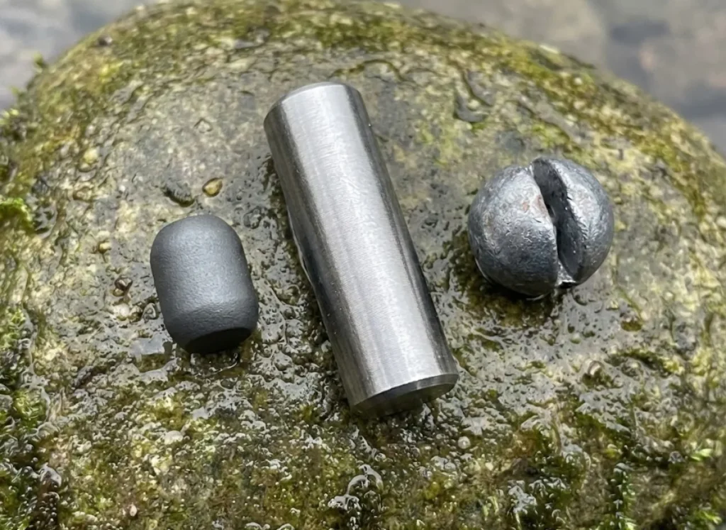 Three different fishing weights—tungsten, steel, and tin—sitting on a wet river rock to compare size and density.