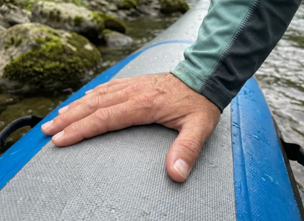 Close up of a hand pressing on a rigid drop-stitch inflatable boat floor to test stability.