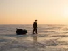 Ice Fishing Basics: Mastering Safety, Gear & Workflow A lone ice angler pulling a sled across a frozen lake at sunrise, demonstrating the vast and harsh environment of ice fishing.