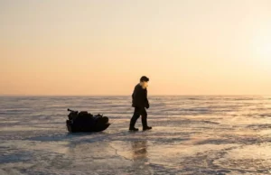 Ice Fishing Basics: Mastering Safety, Gear & Workflow A lone ice angler pulling a sled across a frozen lake at sunrise, demonstrating the vast and harsh environment of ice fishing.