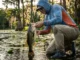 Largemouth Bass Facts: A Tactical Biology Guide Angler kneeling in water holding a large bass, examining its anatomy before releasing it into a lake with lily pads.