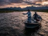 Best Fly Fishing Rivers Montana: Ranked by Difficulty A wide angle view of a drift boat on a large Montana river at sunset with mountains in the background.