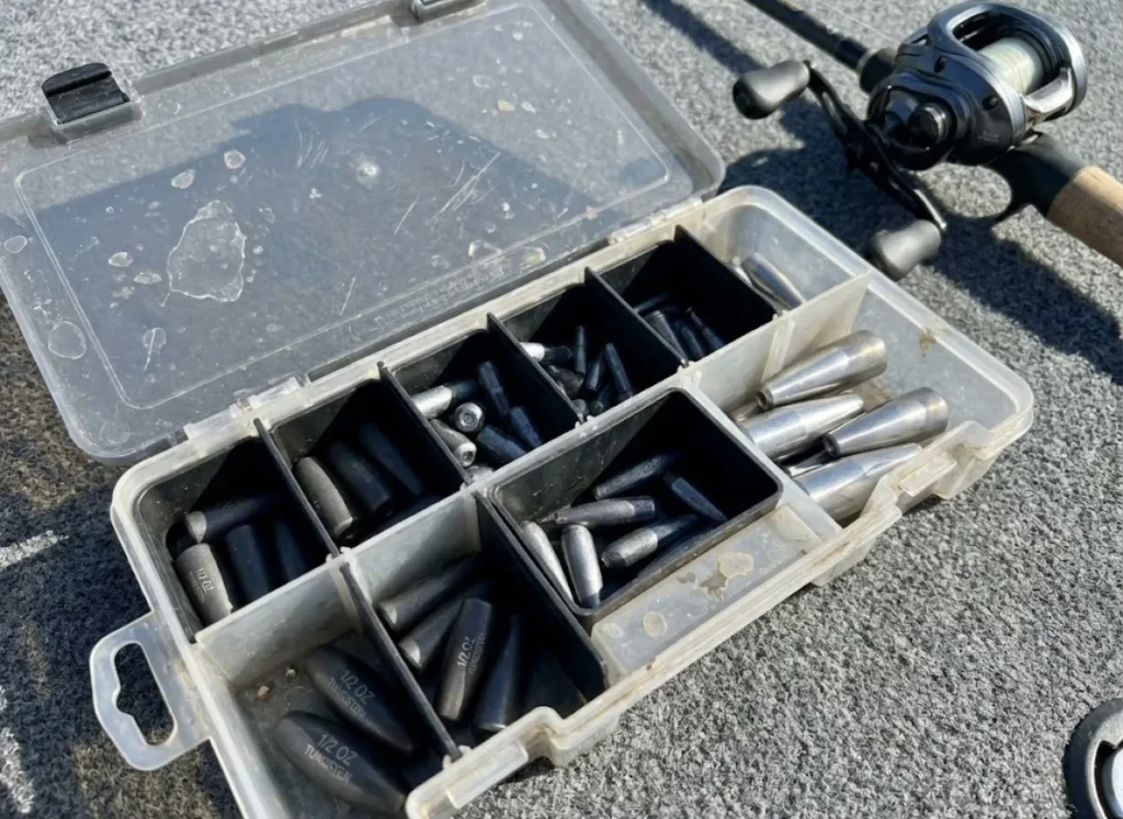 An open tackle box on a boat deck filled with organized tungsten and steel fishing weights.