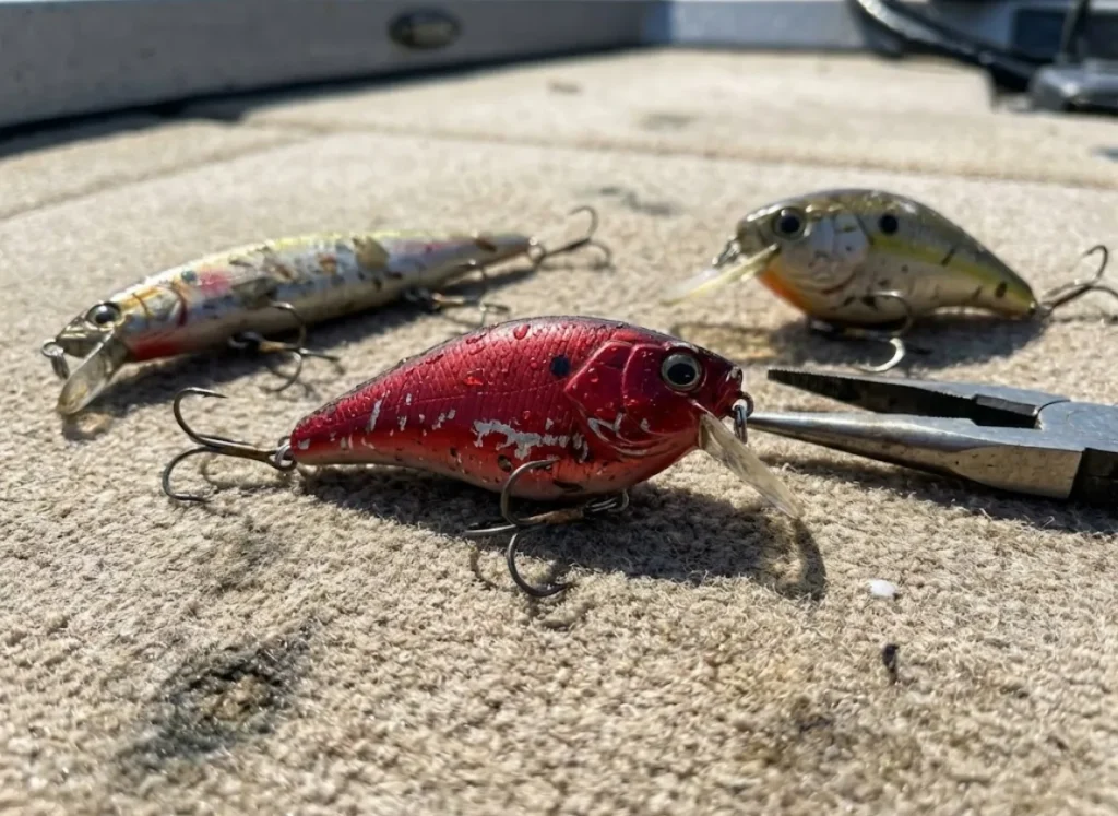Close-up of used suspending jerkbait, red lipless crankbait, and squarebill crankbait on boat carpet.