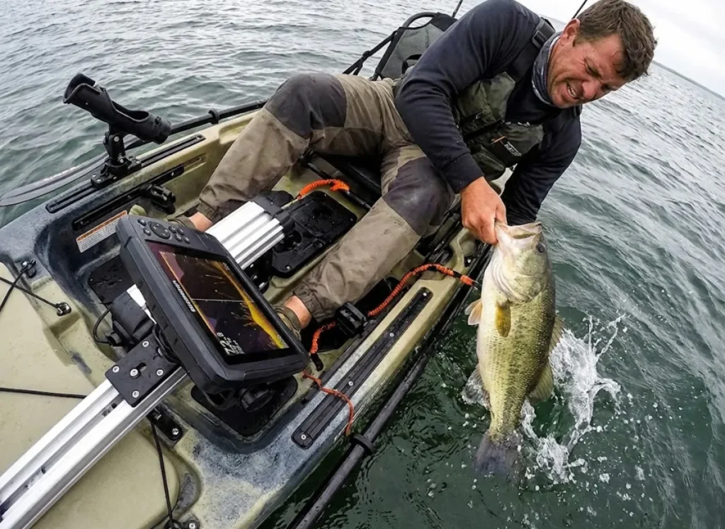 A kayak angler landing a fish with a mounted fish finder visible in the foreground.