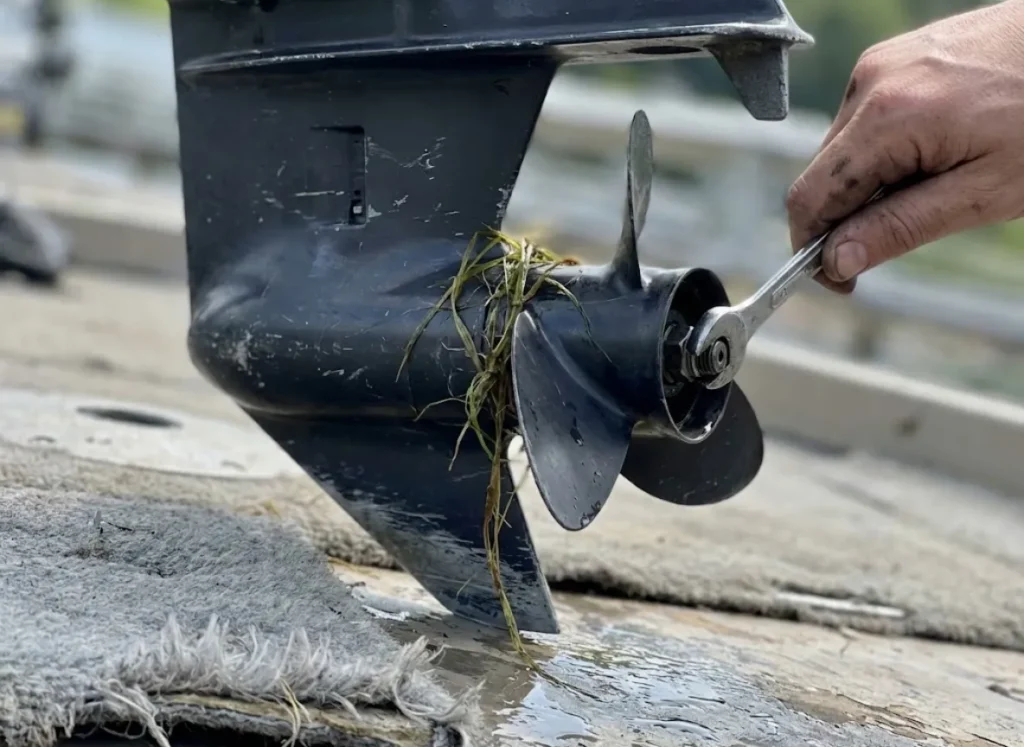 Close up of a mechanic's hand adjusting a trolling motor propeller with visible signs of wear and tear.