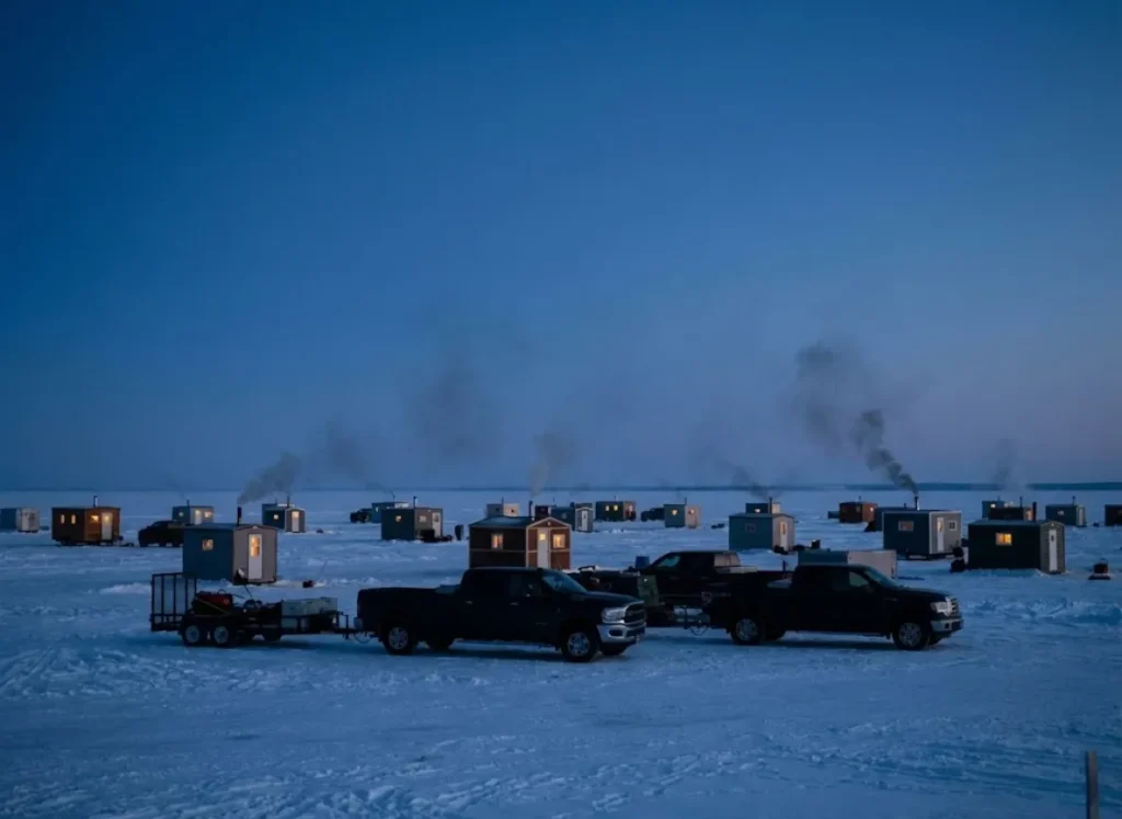 A sprawl of ice fishing sleeper shacks and wheelhouses on the frozen horizon of Upper Red Lake at dusk.